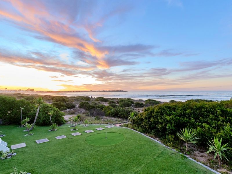 A scenic view of the ocean at sunset, featuring a well-maintained private putting green and landscaped garden area.