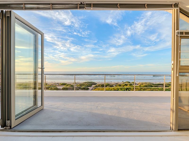 A spacious balcony featuring bi-fold doors and a stainless steel balustrade, offering unobstructed panoramic ocean and beach views.