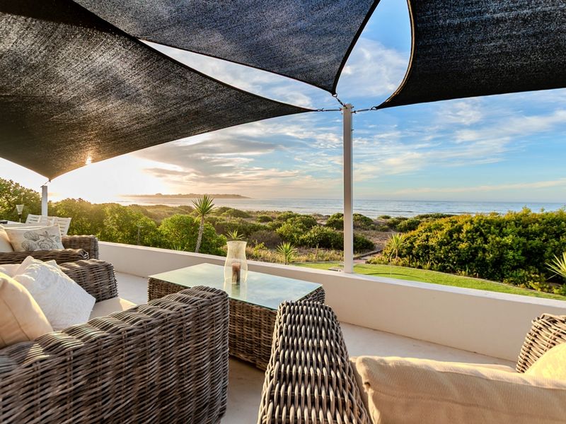 A spacious outdoor patio featuring a protective shade sail, concrete balustrade, and stunning panoramic ocean views.