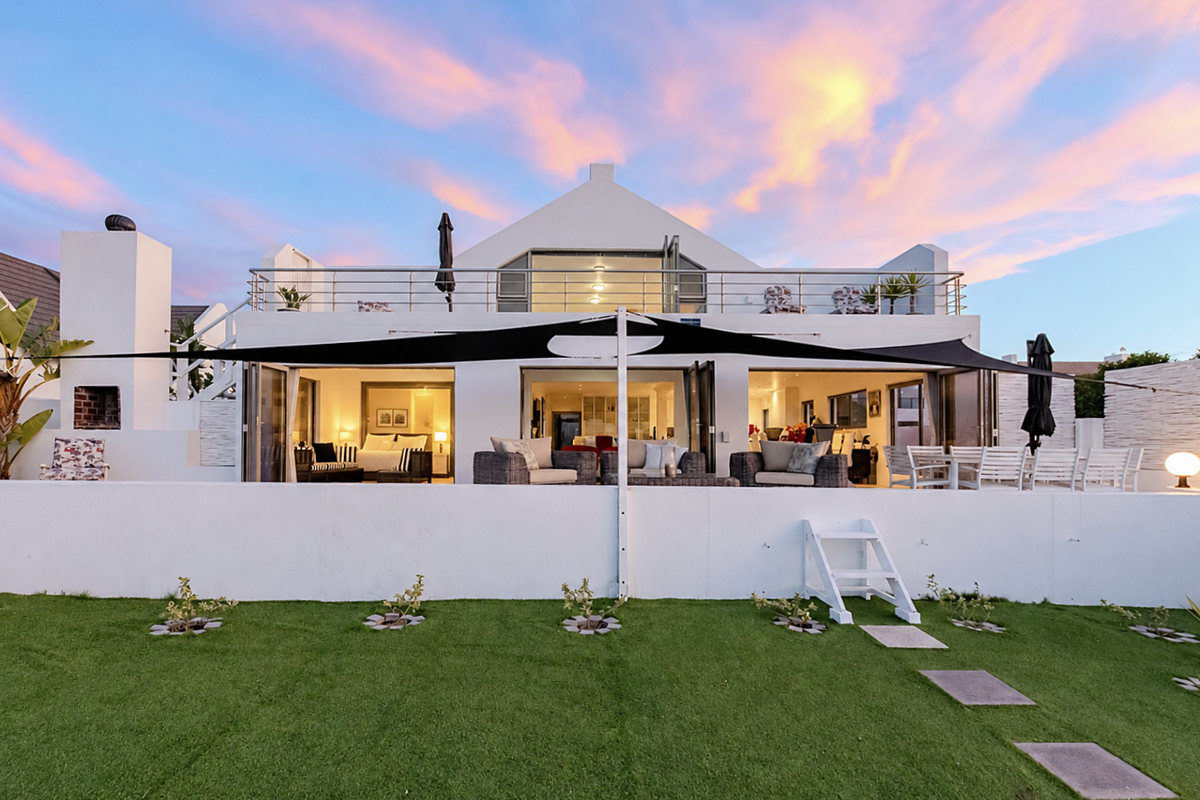 Rear view of a modern double-story home featuring a spacious patio, upper balcony, bi-fold doors, and a well-maintained garden with an outdoor fireplace.