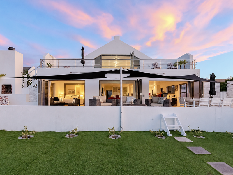 Rear view of a modern double-story home featuring a spacious patio, upper balcony, bi-fold doors, and a well-maintained garden with an outdoor fireplace.