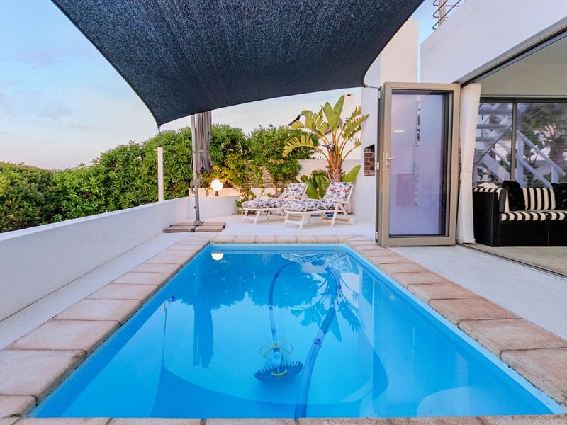 A well-maintained outdoor pool area featuring a shade sail, tiled coping, and direct access to the interior living space via sliding glass doors.