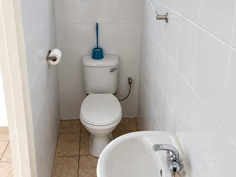 Compact bathroom featuring white wall tiles, a wall-mounted basin, and a standard toilet, requiring minor cosmetic updates to refresh the space.