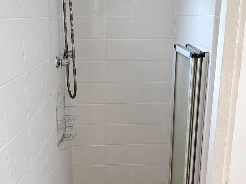 A compact shower stall featuring white wall tiles, a mosaic-style tiled floor, and a folding shower screen.