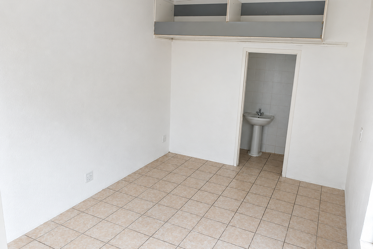 A vacant bedroom featuring tiled flooring, built-in overhead storage shelving, and an en-suite area with a pedestal basin.