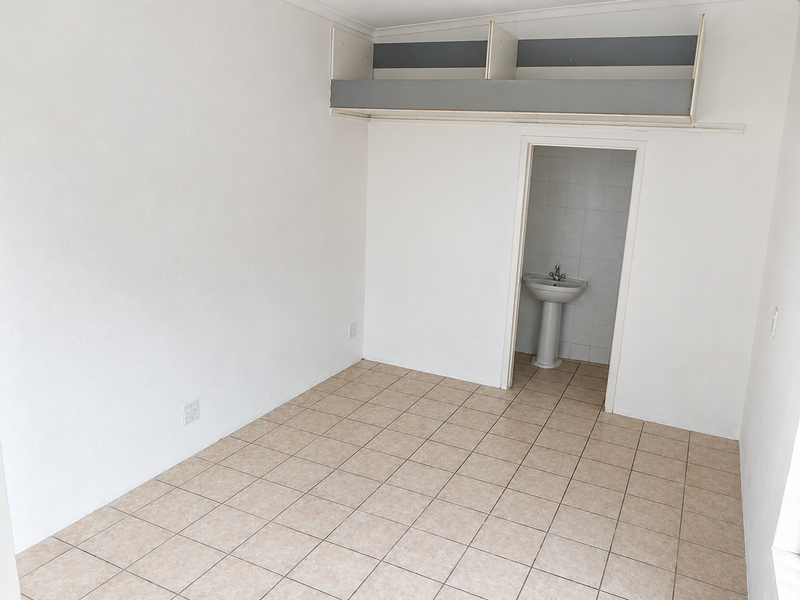 A vacant bedroom featuring tiled flooring, built-in overhead storage shelving, and an en-suite area with a pedestal basin.