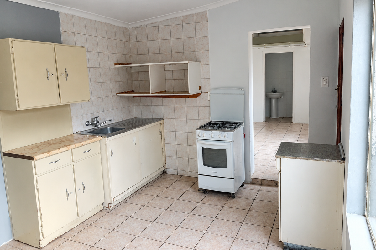 A functional kitchen featuring tiled flooring, built-in cabinetry, a stainless steel sink, and a freestanding gas stove, with an adjacent view of a bathroom.