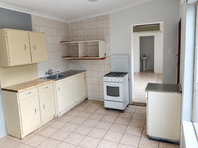 A functional kitchen featuring tiled flooring, built-in cabinetry, a stainless steel sink, and a freestanding gas stove, with an adjacent view of a bathroom.