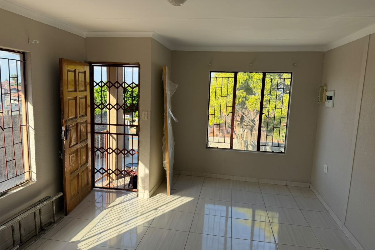 A bright, empty living area featuring neutral tiled flooring, security gates, and large windows with burglar bars, offering a clean canvas for interior design.