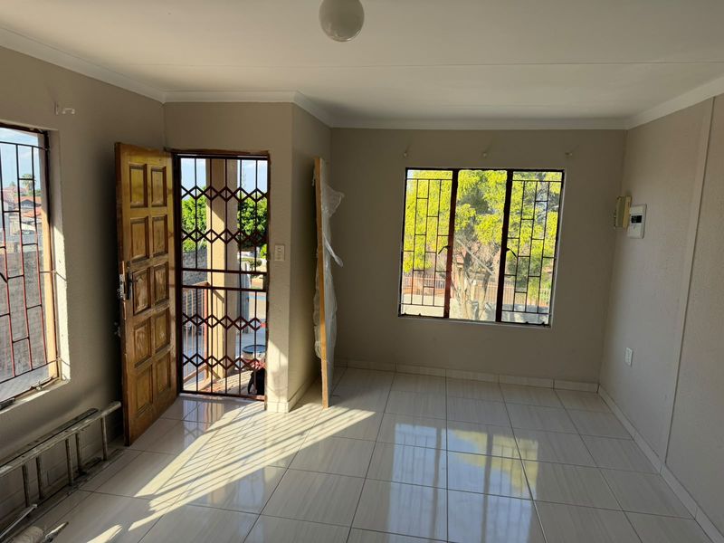 A bright, empty living area featuring neutral tiled flooring, security gates, and large windows with burglar bars, offering a clean canvas for interior design.