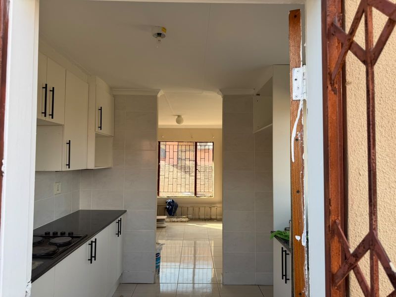 A functional kitchen featuring white cabinetry, dark granite countertops, and tiled finishes, leading into an adjacent living area with natural light.