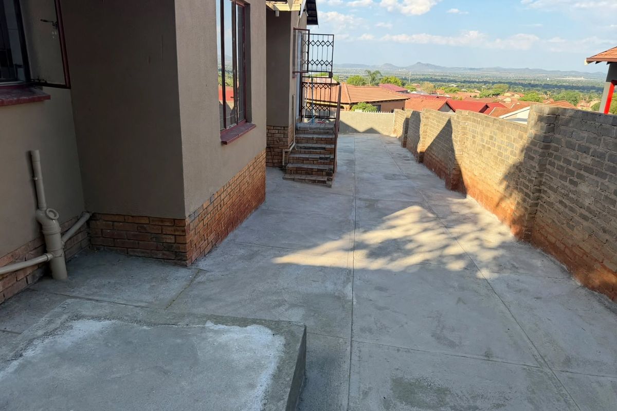 Rear exterior area featuring concrete paving, a brick boundary wall, and an external staircase with scenic views of the surrounding neighborhood.