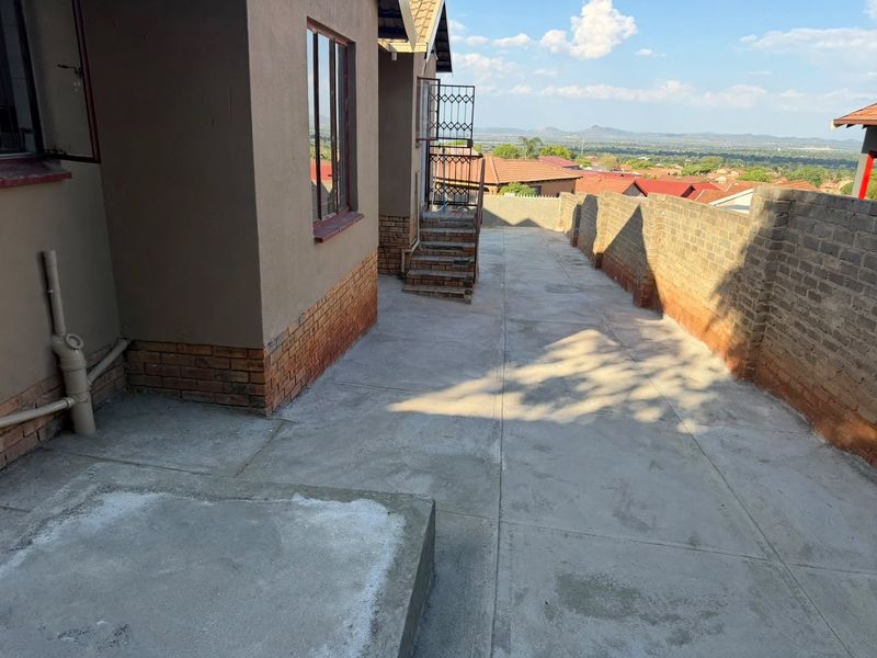 Rear exterior area featuring concrete paving, a brick boundary wall, and an external staircase with scenic views of the surrounding neighborhood.