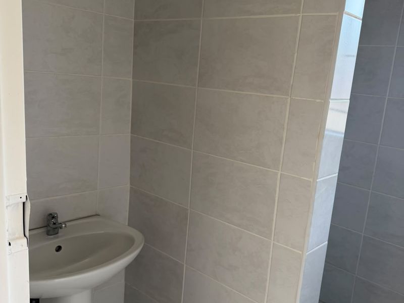 A functional bathroom featuring a pedestal basin and a tiled shower enclosure with neutral ceramic wall and floor tiles.
