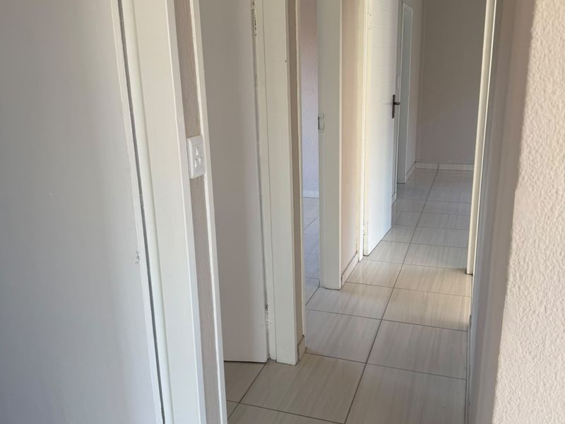 A functional hallway featuring tiled flooring and multiple internal doors, with a visible ceiling access hatch requiring a cover.