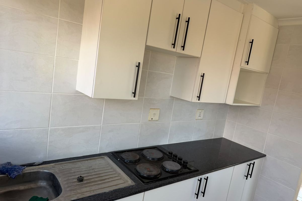 A functional kitchen featuring white cabinetry, black granite countertops, a stainless steel sink, and an integrated electric hob with tiled wall finishes.