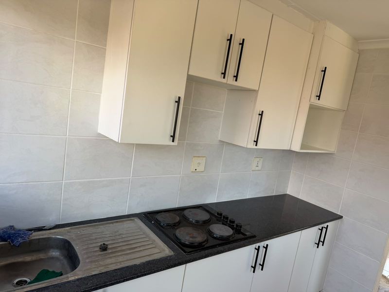 A functional kitchen featuring white cabinetry, black granite countertops, a stainless steel sink, and an integrated electric hob with tiled wall finishes.