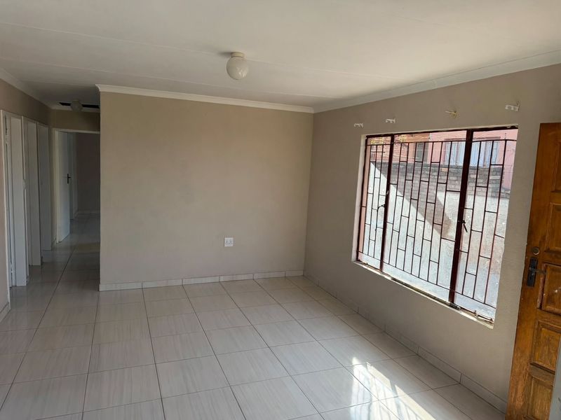An empty living room featuring neutral tiled flooring, coved ceilings, and a window fitted with security bars.