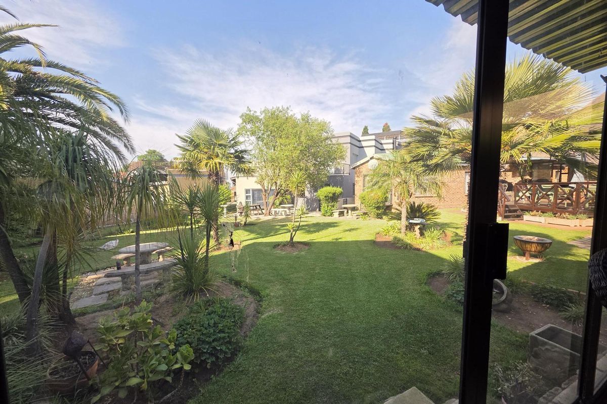 A view of a well-maintained rear garden with lush lawn, mature palm trees, and established landscaping, viewed from an interior sliding door.