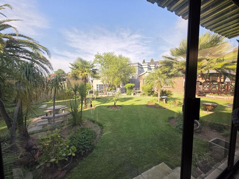 A view of a well-maintained rear garden with lush lawn, mature palm trees, and established landscaping, viewed from an interior sliding door.