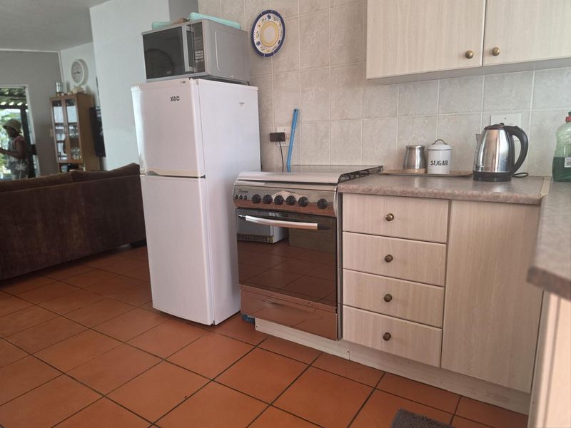 A functional kitchen featuring laminate cabinetry, tiled backsplash, and tiled flooring, with an integrated open-plan layout connecting to the living area.