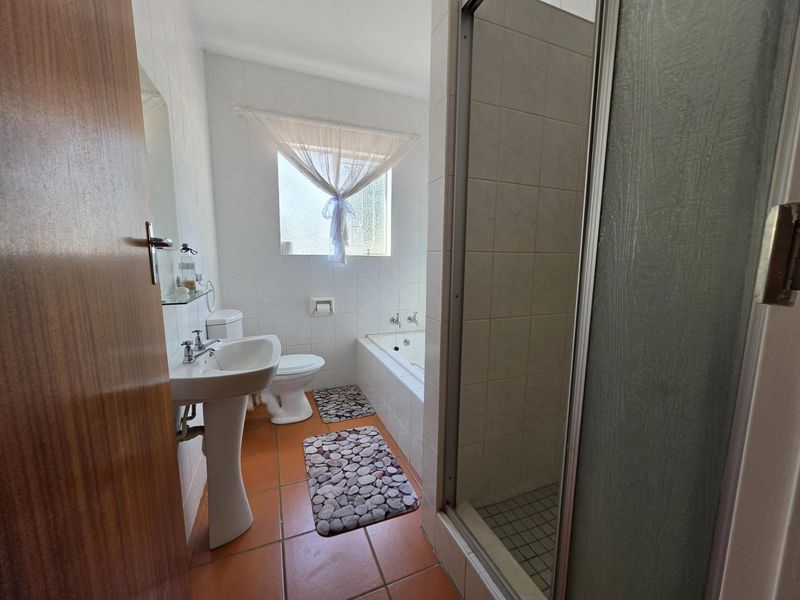 A functional bathroom featuring a pedestal basin, toilet, built-in bathtub, and a separate shower enclosure with tiled finishes throughout.