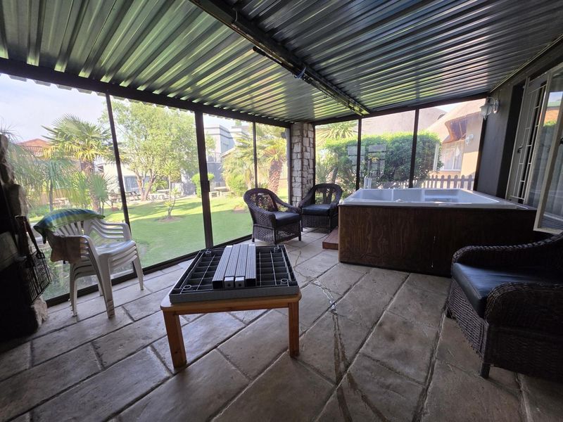 Enclosed patio area featuring a corrugated metal roof, stone accents, paved flooring, and a built-in hot tub overlooking the garden.