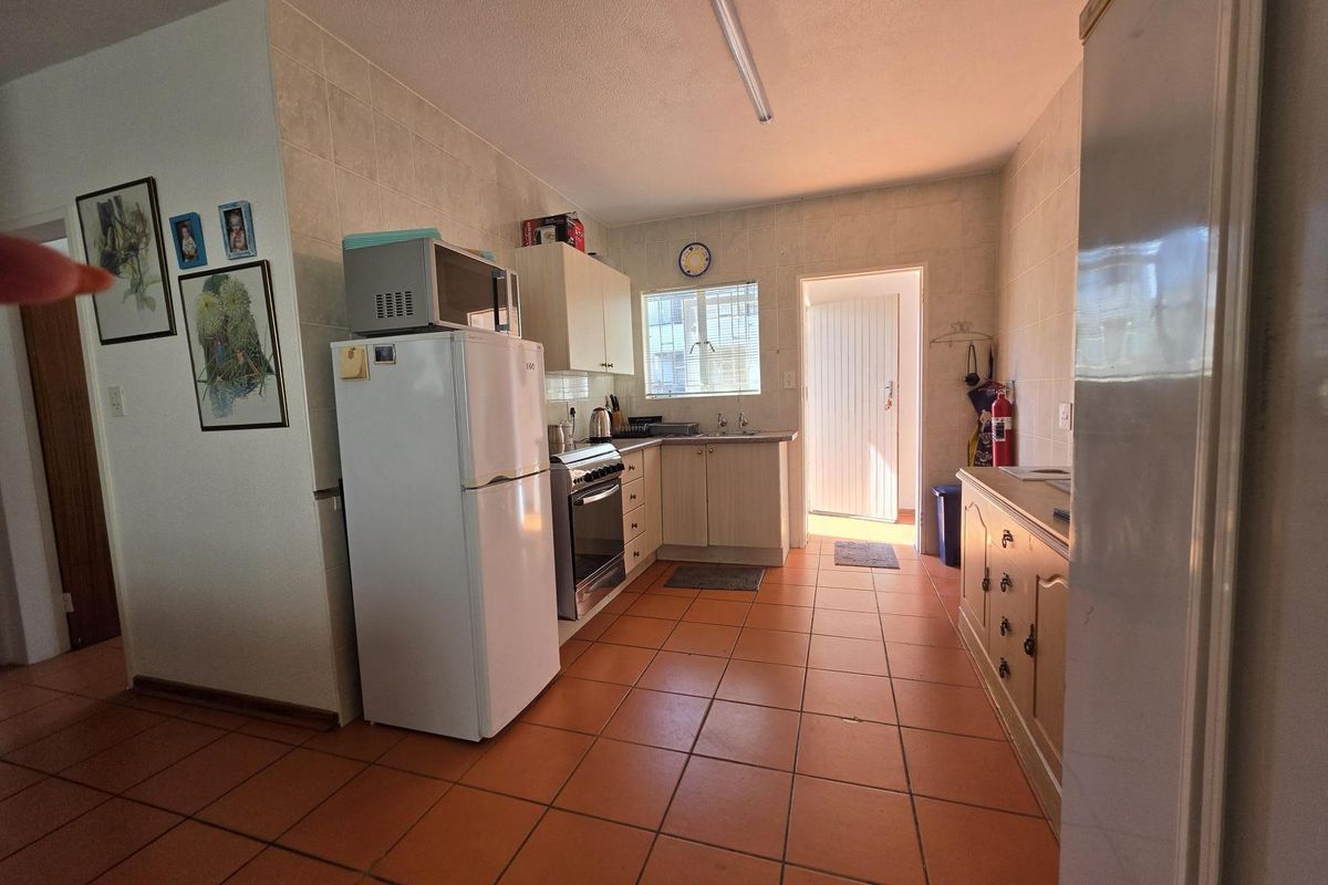 A functional kitchen featuring tiled flooring, wall-to-wall tiling, built-in cabinetry, and a freestanding stove, with direct access to an exterior door.
