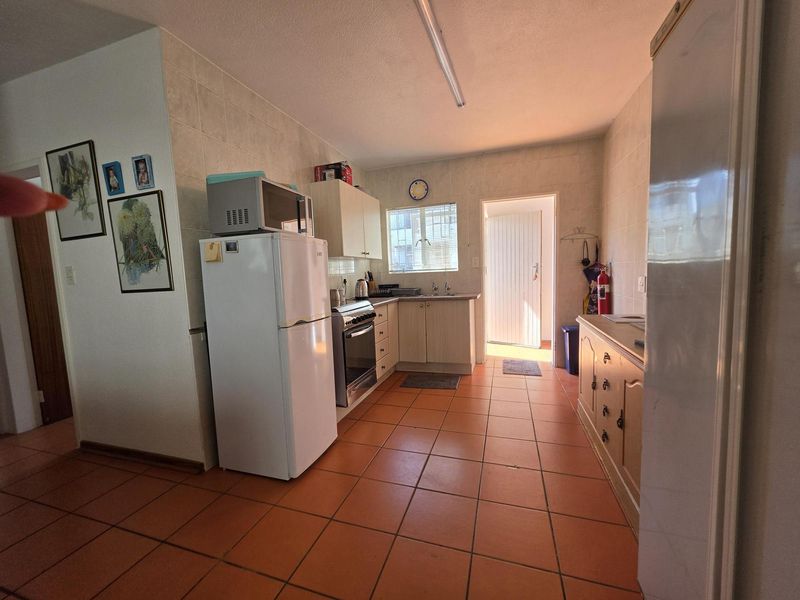 A functional kitchen featuring tiled flooring, wall-to-wall tiling, built-in cabinetry, and a freestanding stove, with direct access to an exterior door.
