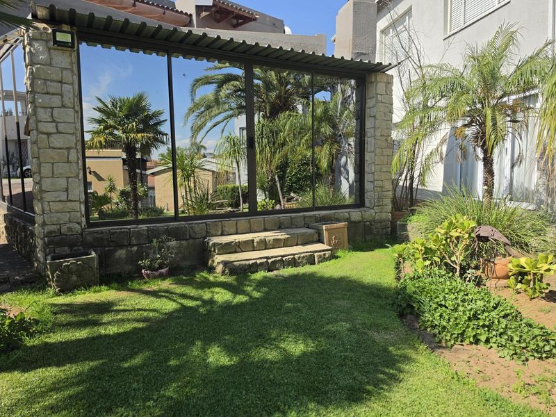 A covered patio area featuring stone masonry walls, sliding glass doors, and stone steps leading to a landscaped garden.