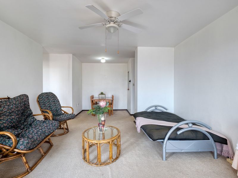 An open-plan living and dining area featuring neutral wall finishes, carpeted flooring, and a ceiling fan, providing a versatile space for relaxation and meals.