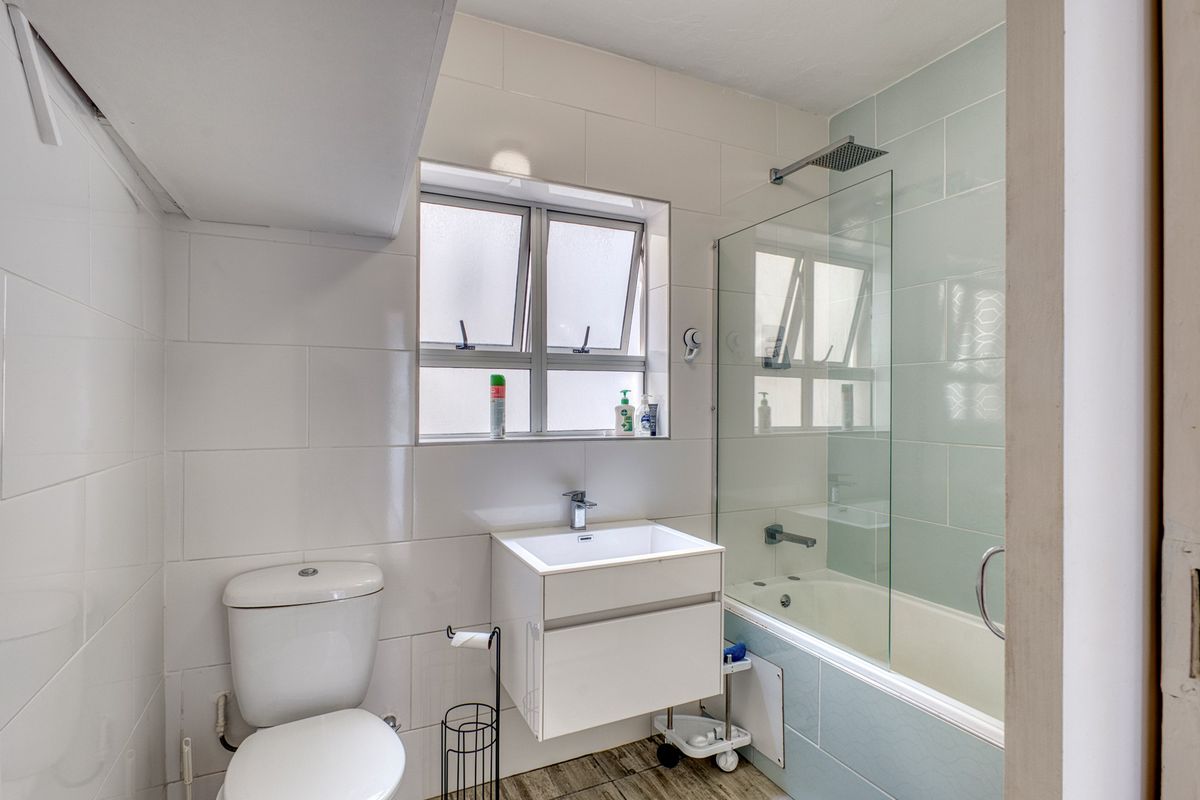 A clean, modern bathroom featuring a wall-mounted vanity, a bathtub with a glass shower screen, and neutral tiled walls.