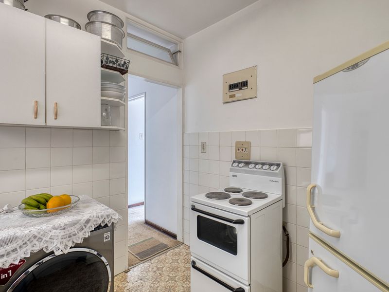 A compact, functional kitchen featuring tiled splashbacks, built-in cabinetry, and a freestanding electric stove, offering potential for modernization.