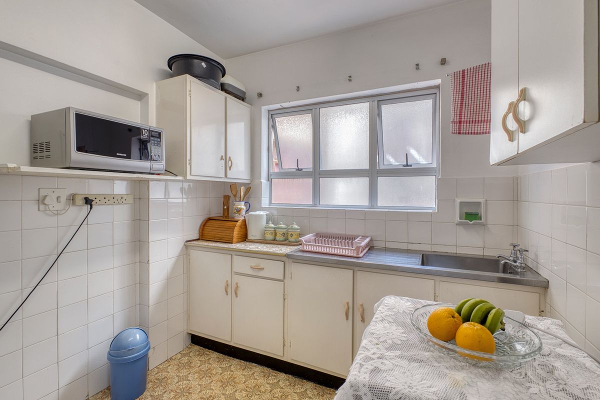 A compact kitchen featuring original cabinetry, a stainless steel sink, tiled backsplash, and a window providing natural light.