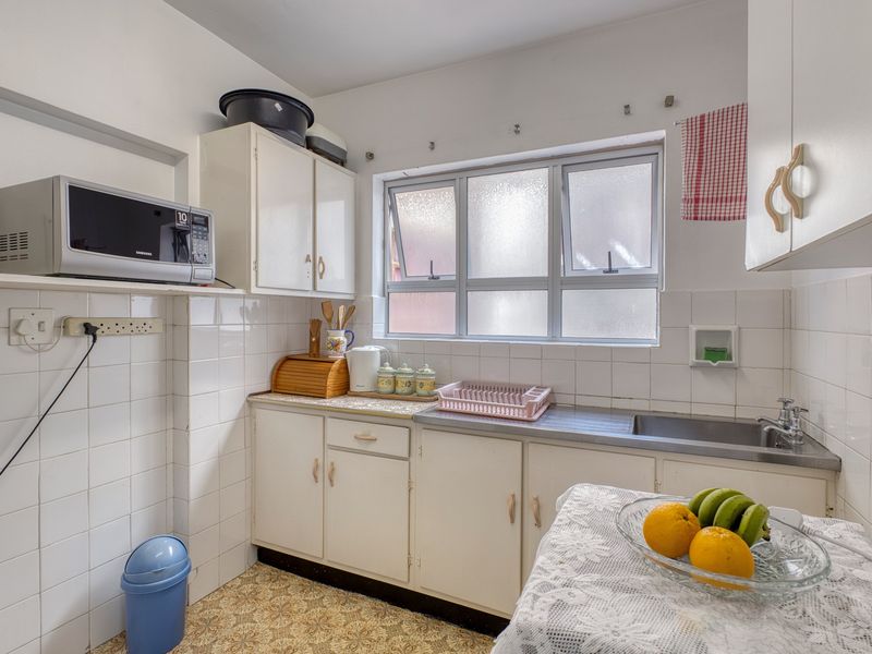 A compact kitchen featuring original cabinetry, a stainless steel sink, tiled backsplash, and a window providing natural light.