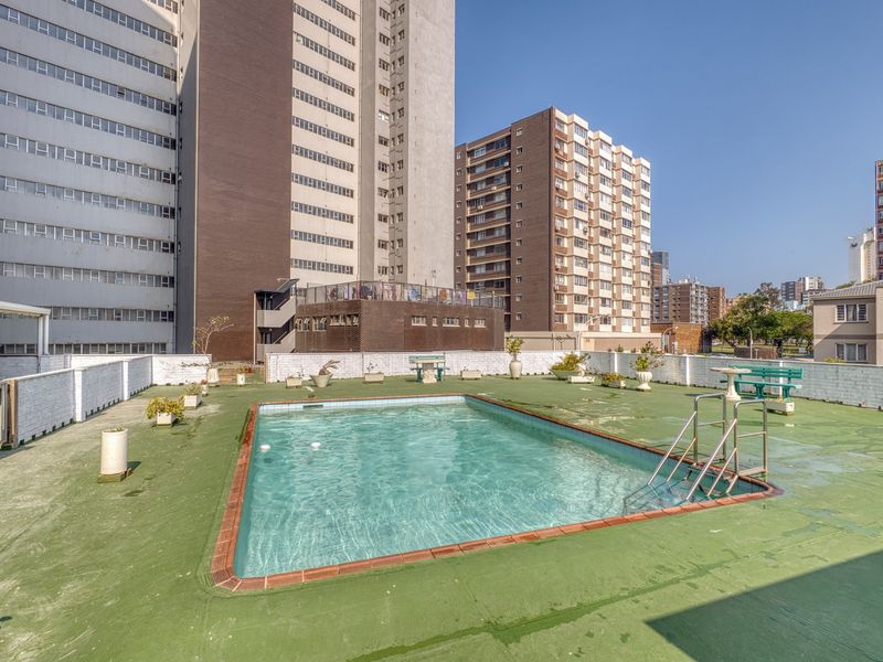 Communal rooftop swimming pool area featuring a paved deck and perimeter wall, situated within an apartment complex setting.