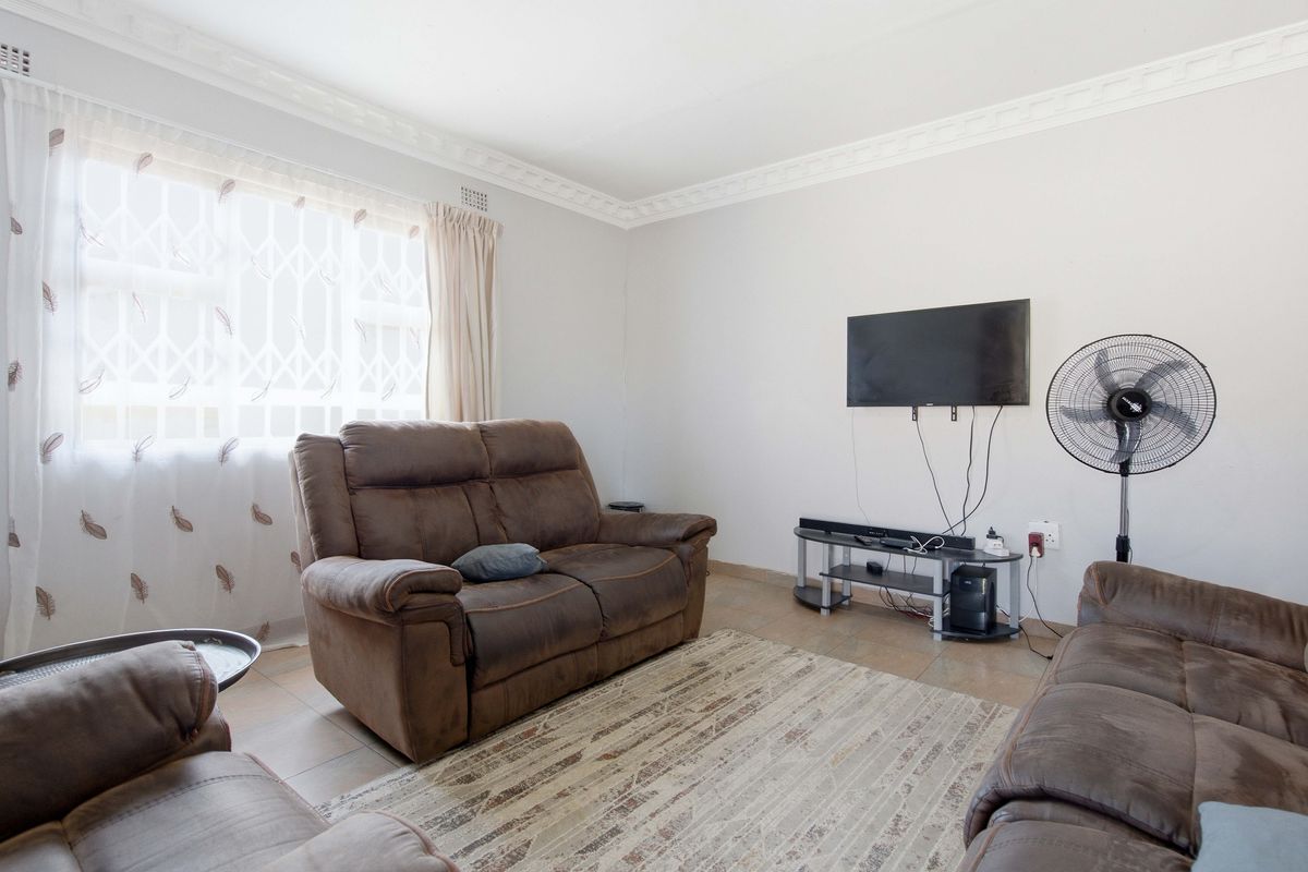 A living room featuring tiled flooring and decorative ceiling cornicing, with a window fitted with a security gate.
