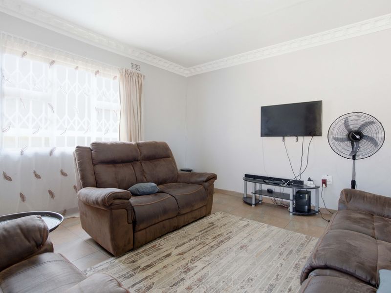 A living room featuring tiled flooring and decorative ceiling cornicing, with a window fitted with a security gate.