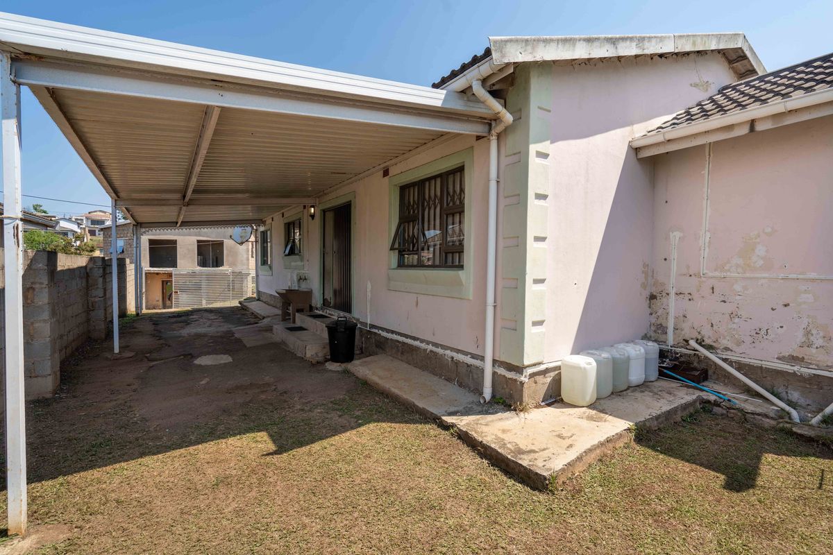 Rear exterior view of the property featuring a covered carport, security bars on windows, and a concrete apron with visible wear to exterior finishes.