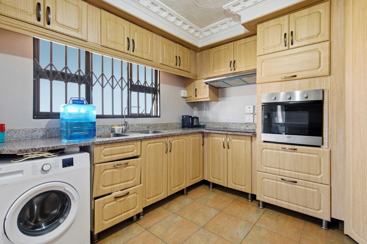 Functional kitchen featuring light wood cabinetry, granite countertops, built-in oven, extractor fan, and tiled flooring with a security-fitted window.