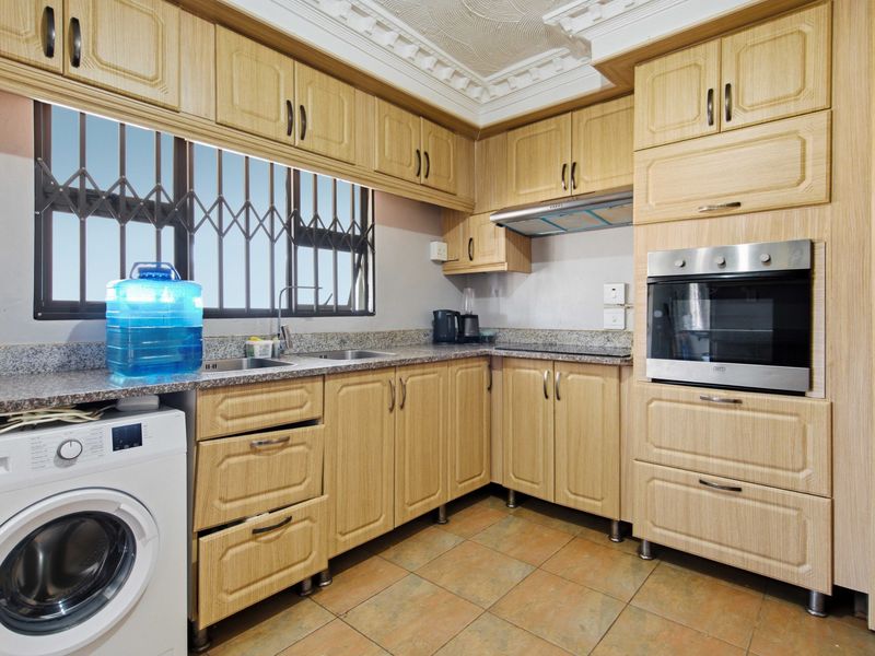 Functional kitchen featuring light wood cabinetry, granite countertops, built-in oven, extractor fan, and tiled flooring with a security-fitted window.