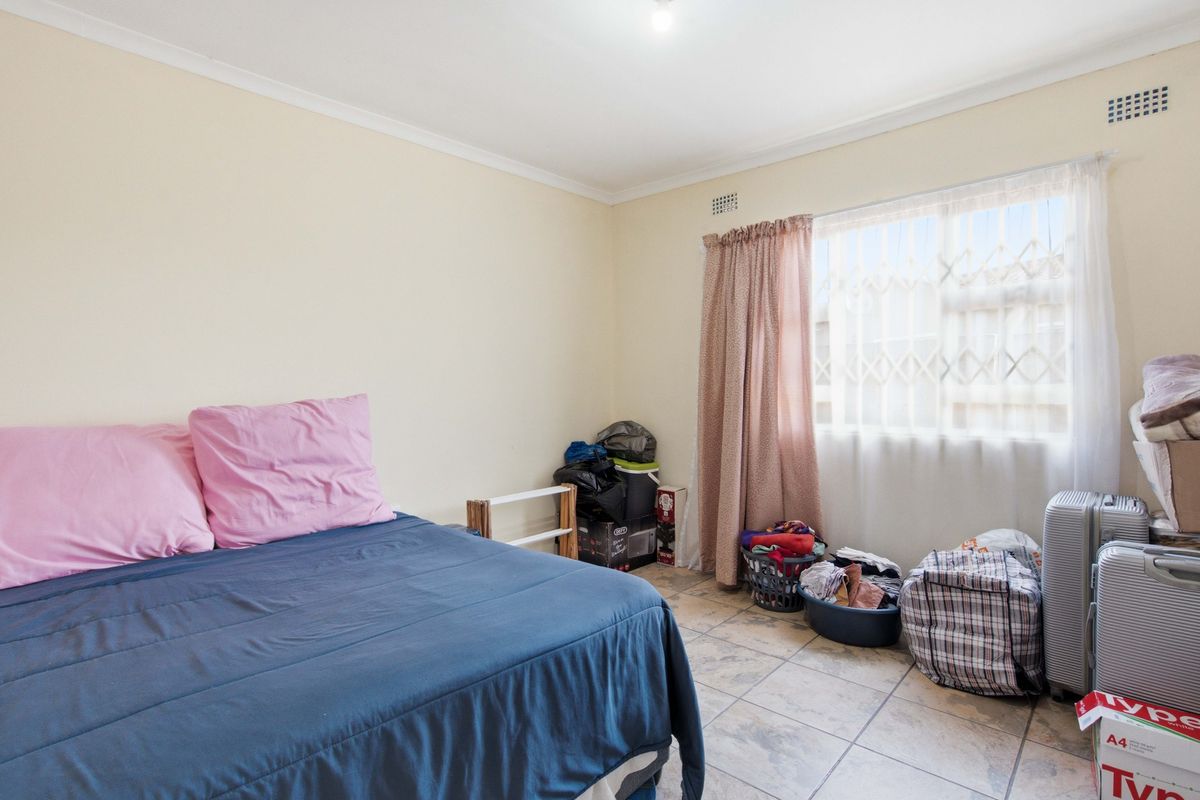 A functional bedroom featuring tiled flooring, a window with a security gate, and neutral wall finishes.