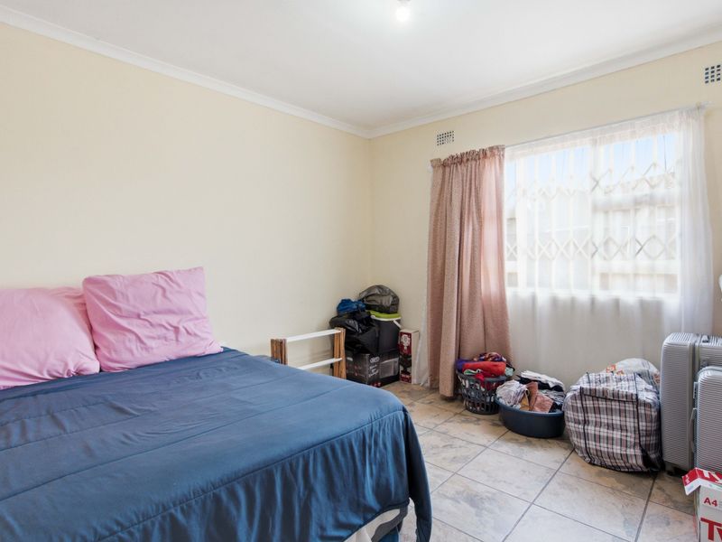 A functional bedroom featuring tiled flooring, a window with a security gate, and neutral wall finishes.
