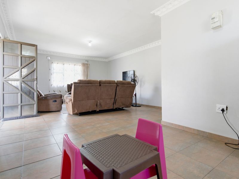 Spacious living area featuring neutral tiled flooring, decorative ceiling cornicing, and a security gate leading to the exterior.