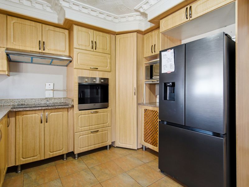 A functional kitchen featuring light wood cabinetry, granite countertops, built-in oven, extractor fan, and decorative ceiling cornices with tiled flooring.