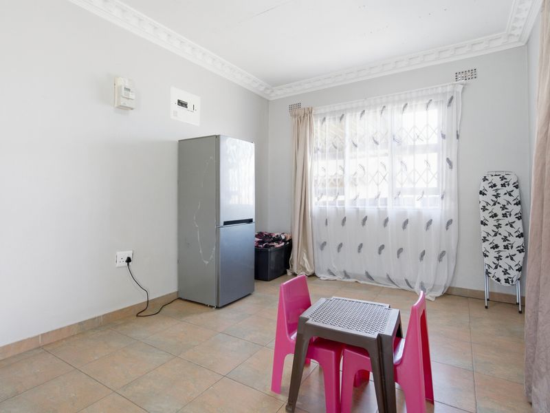 A functional living area featuring tiled flooring, decorative ceiling cornicing, and a window fitted with a security gate.