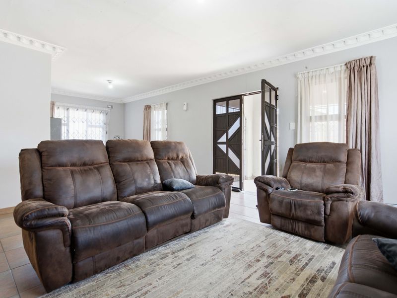 Spacious living room featuring tiled flooring, decorative crown molding, and secure access points with security gates and window bars.