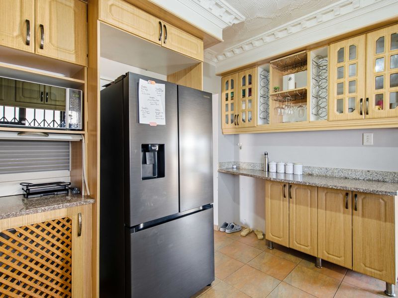 A functional kitchen featuring light wood cabinetry, granite countertops, built-in microwave, and decorative ceiling cornices with tiled flooring.