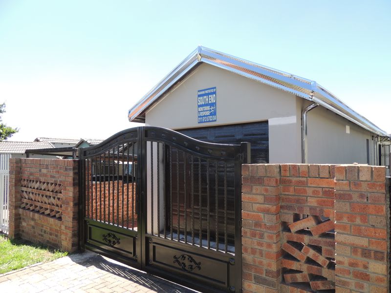 A secure garage featuring a metal door, enclosed by a decorative brick boundary wall and a black wrought iron gate.