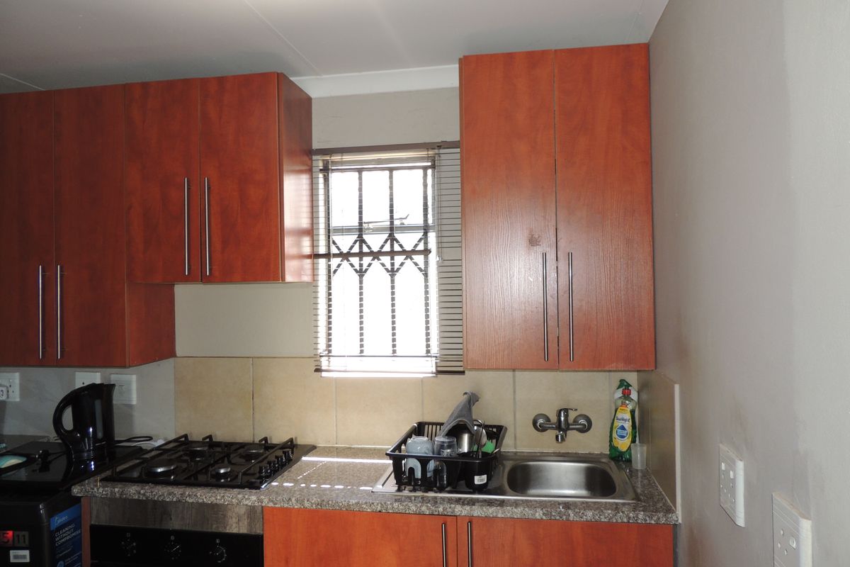 A functional kitchen featuring wood-finish cabinetry, granite countertops, a gas hob, and a stainless steel sink with a window providing natural light.